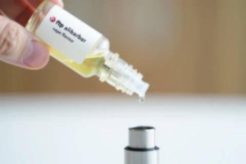 Close up view of a bottle of ftp alibarbar vape flavour liquid being used to refill a vape tank.